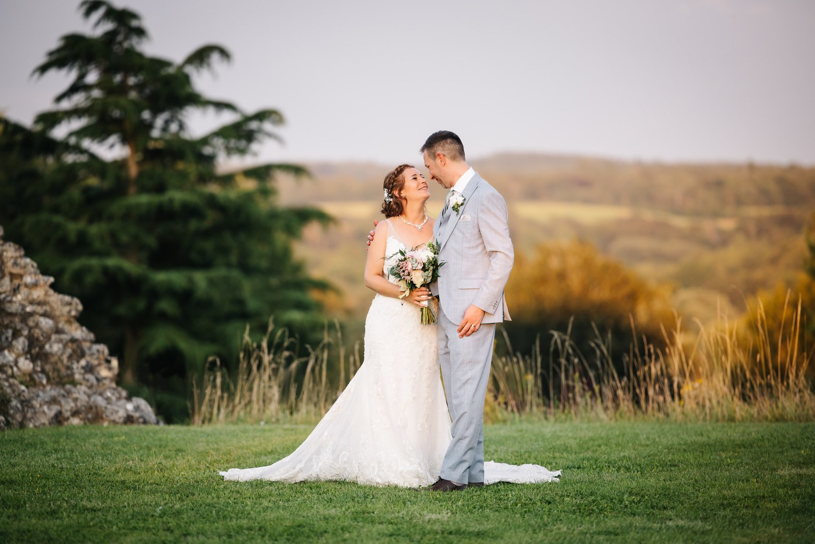 The couple embracing on the lawn at Farnham Castle at golden hour, open countryside beyond