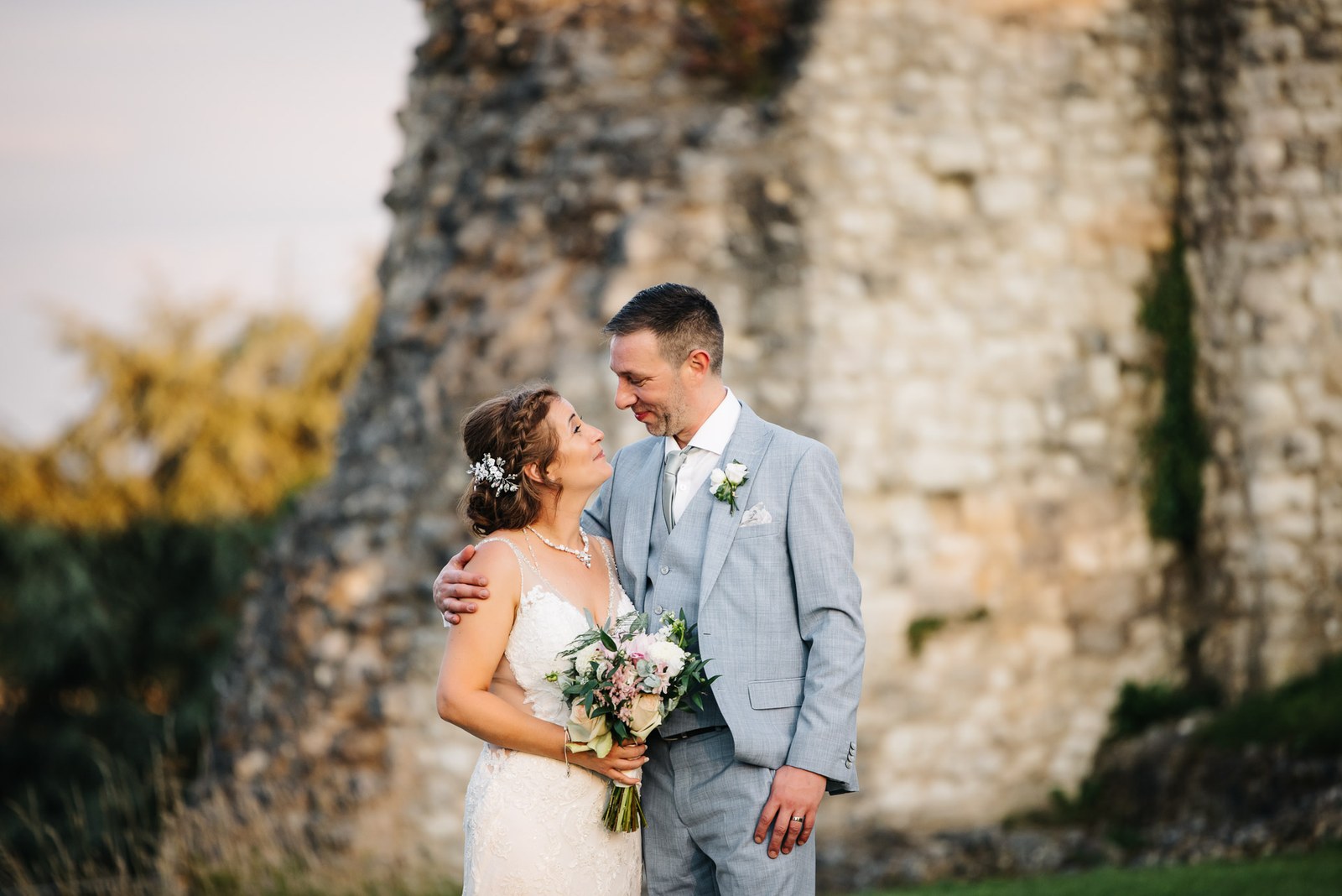 The couple embracing before the ruined stone walls of Farnham Castle in the evening light