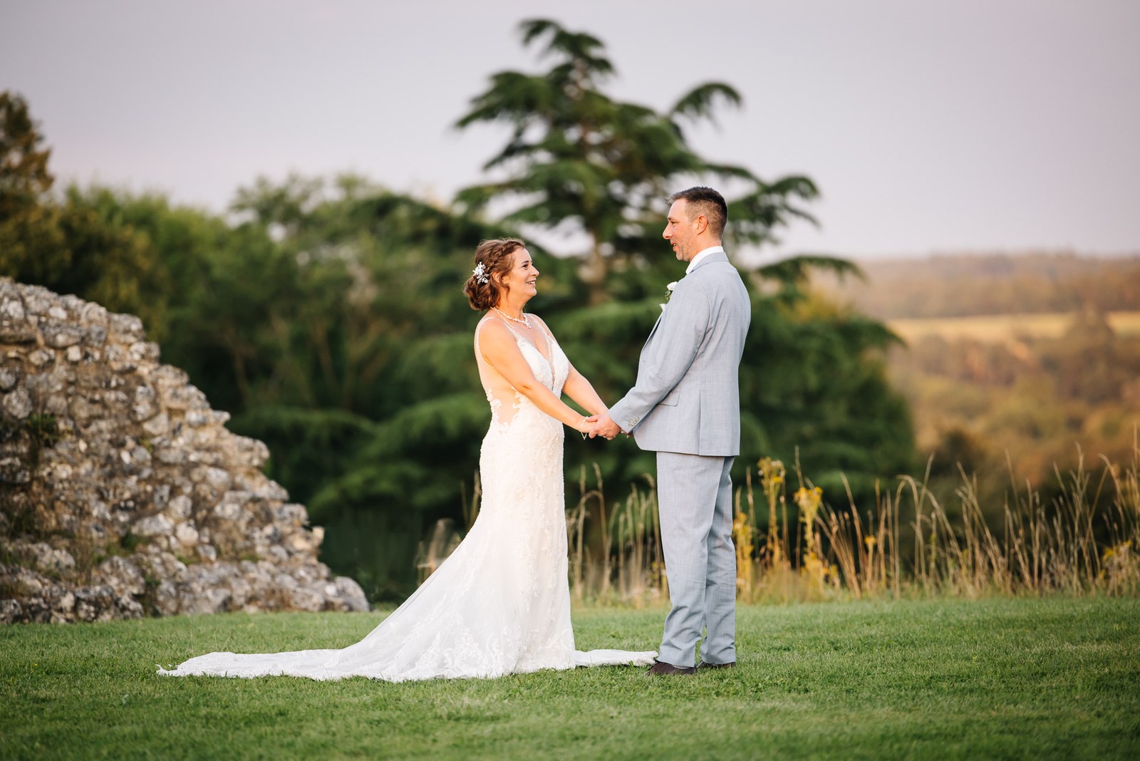 The couple holding hands on the lawn among the castle ruins at golden hour