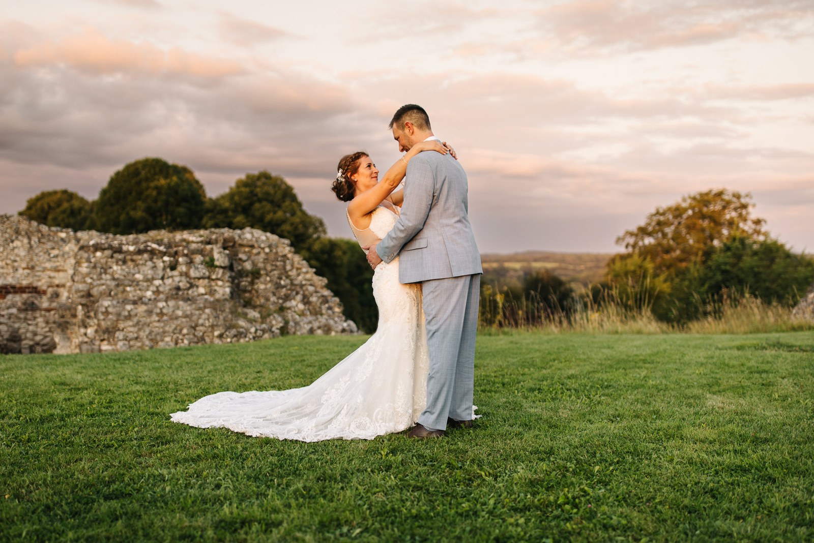 The couple embracing on the lawn at sunset, the castle ruins behind