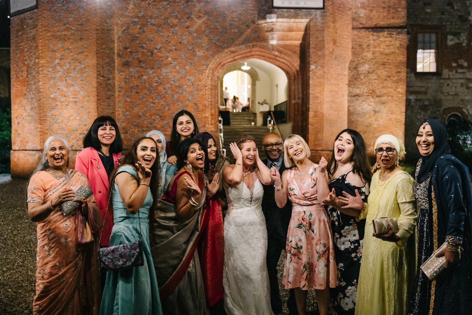 The bride cheering with a group of guests against the brick wall of Farnham Castle