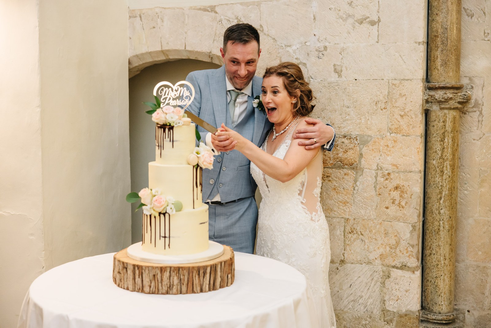 The couple cutting their tiered cake together beneath a stone arch at Farnham Castle