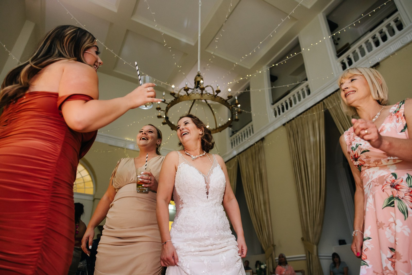 The bride dancing among friends beneath the chandelier and fairy lights