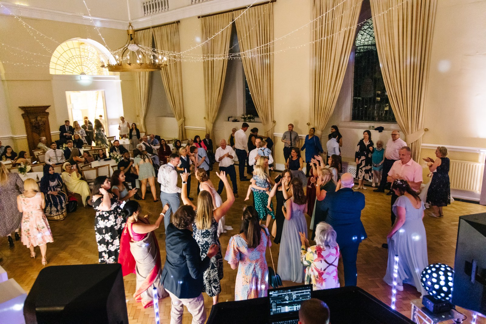 The packed dance floor in the grand reception hall at Farnham Castle, strung with fairy lights