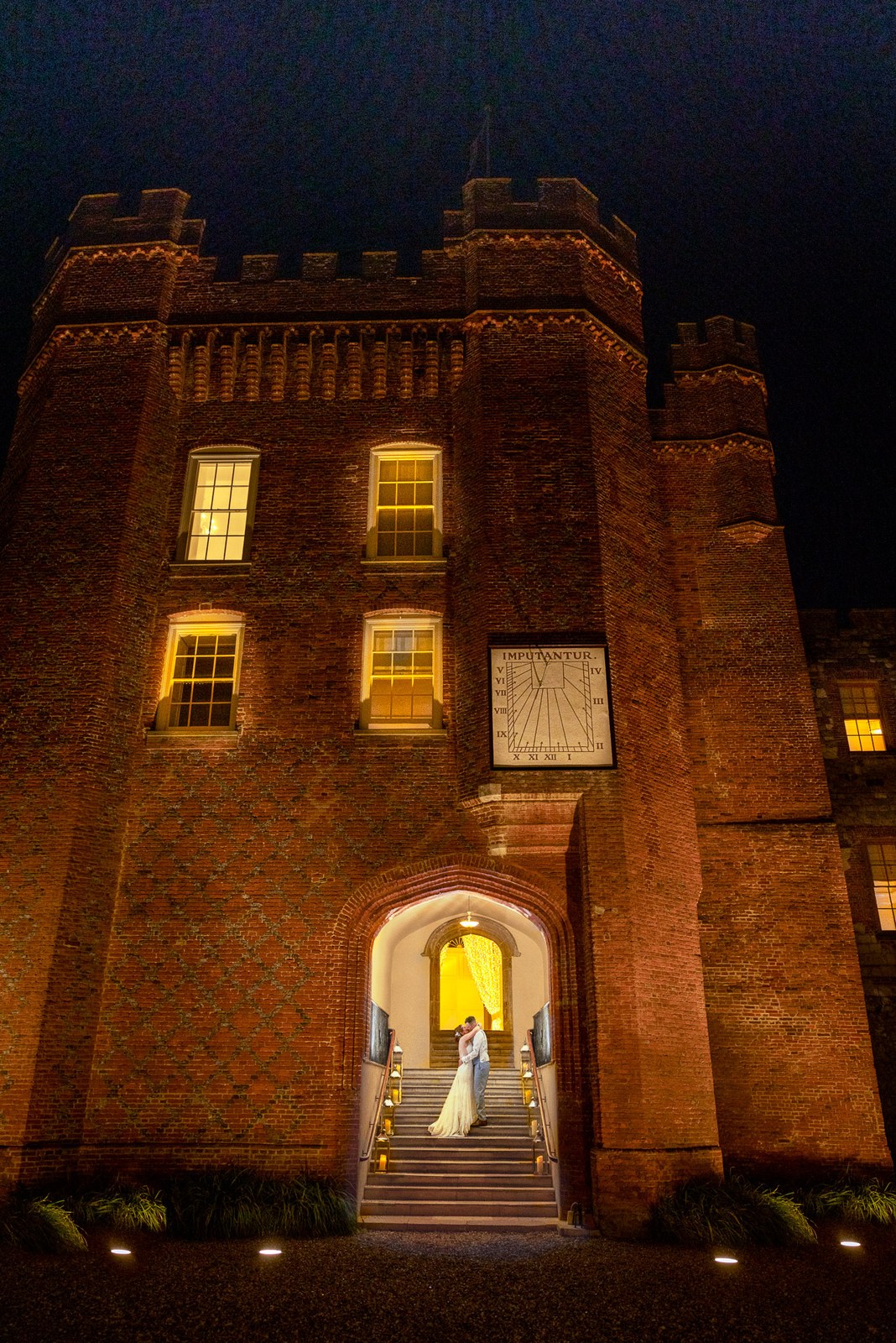 The floodlit brick gatehouse of Farnham Castle at night, the couple in the lit archway