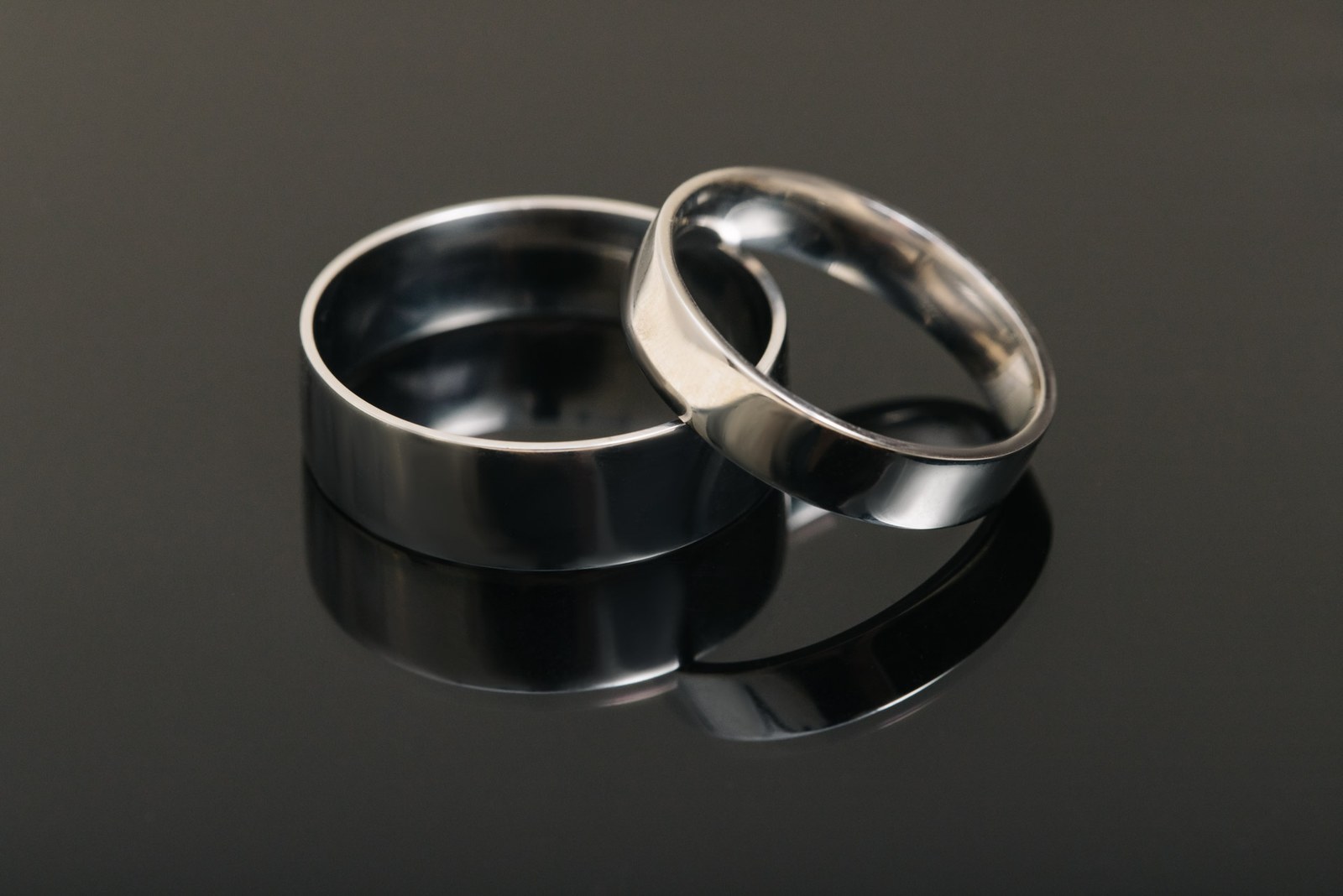 Close-up of the two plain wedding bands on a dark reflective surface