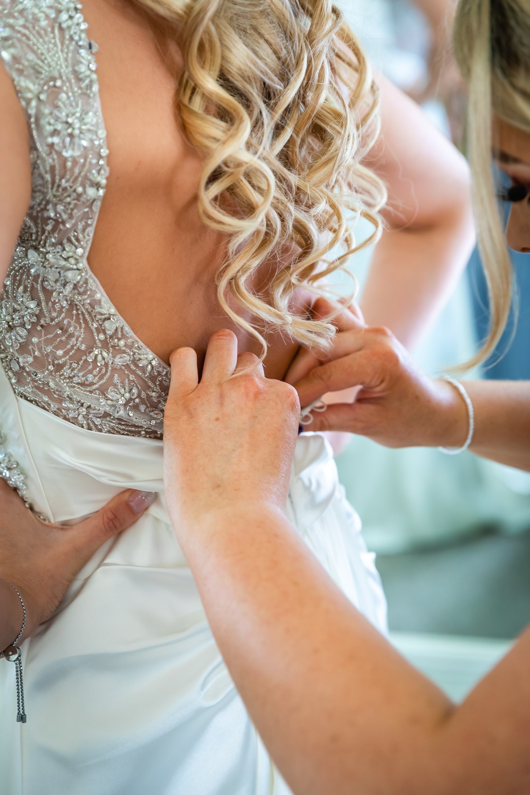 A bridesmaid doing up the beaded back of the bride's ivory gown