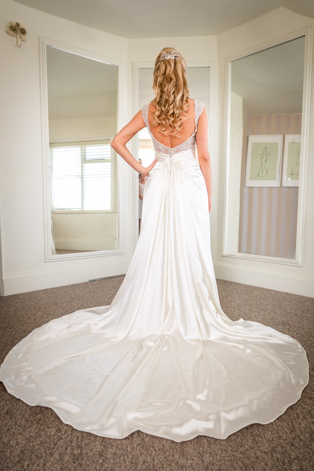 The bride from behind, her satin train fanned out in the bay-window room at Fennes