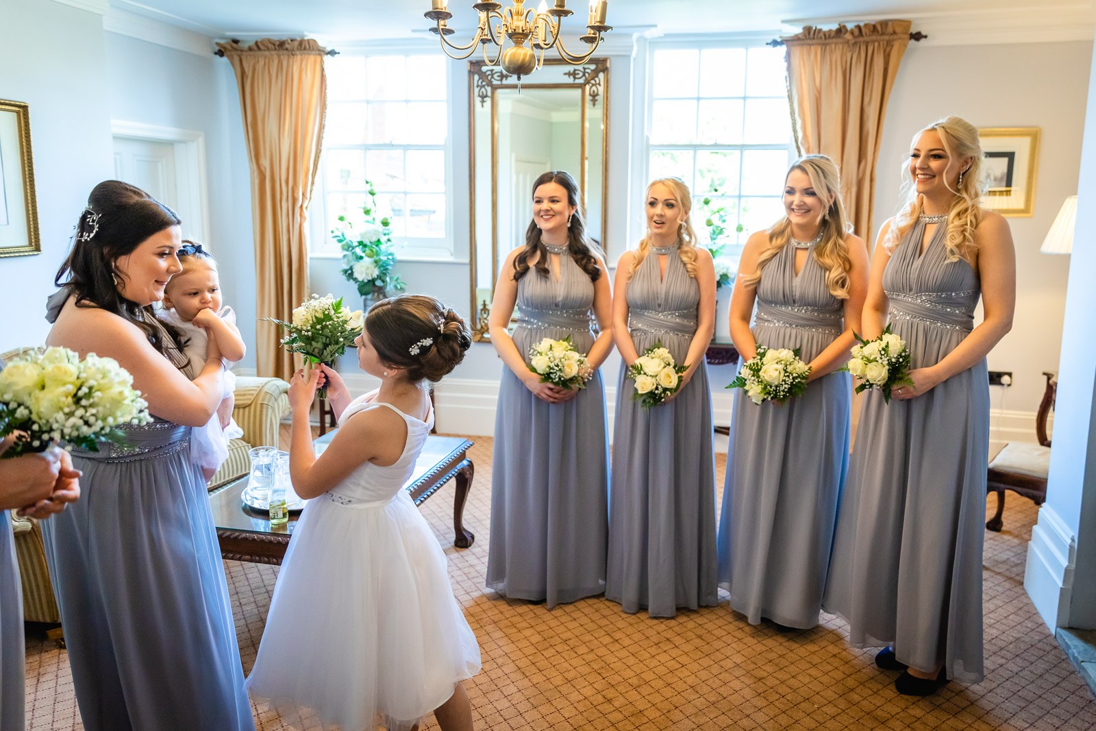 Bridesmaids in lilac with a flower girl and a baby in a bright bay-window room