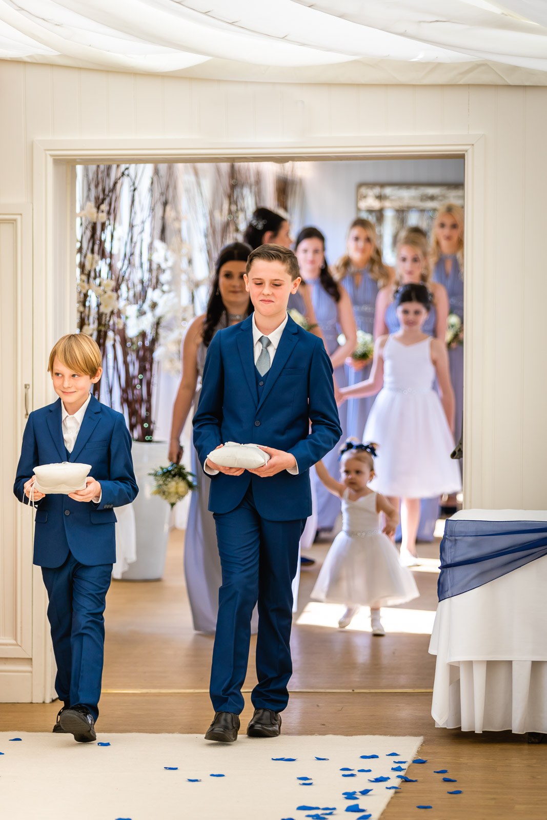 Page boys carrying ring cushions down the aisle, bridesmaids following