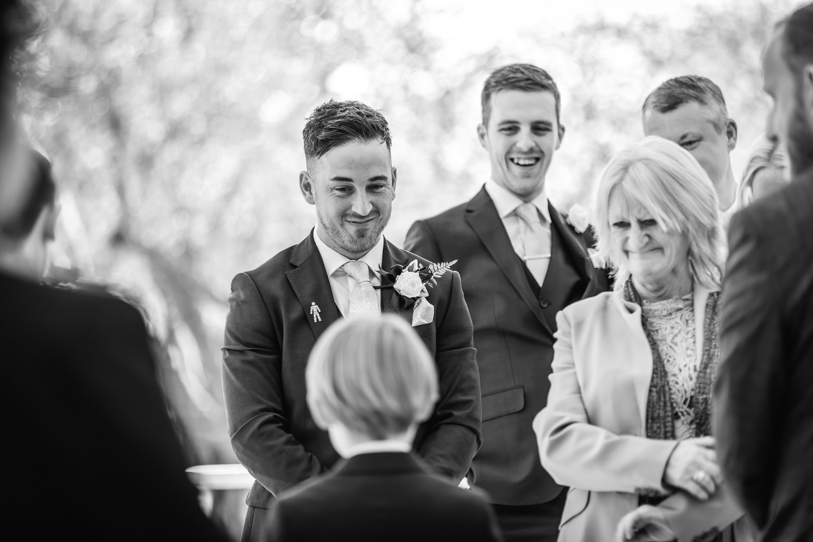 Black-and-white of the groom watching, emotional, a page boy in the foreground