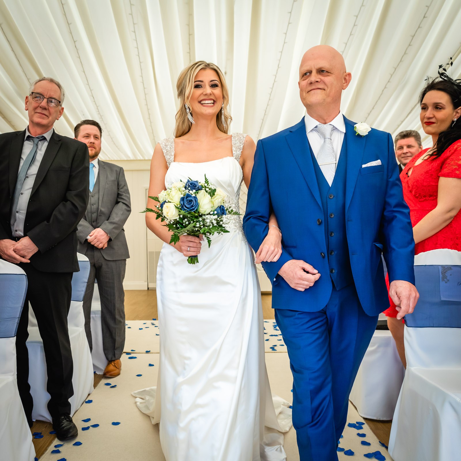 The bride walking down the aisle on her father's arm in the draped ceremony room at Fennes