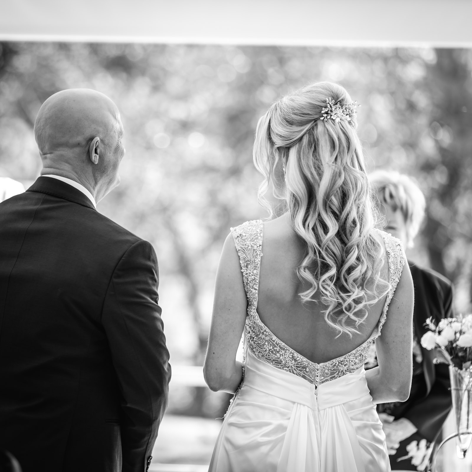 Black-and-white of the bride and her father from behind, her low-back gown