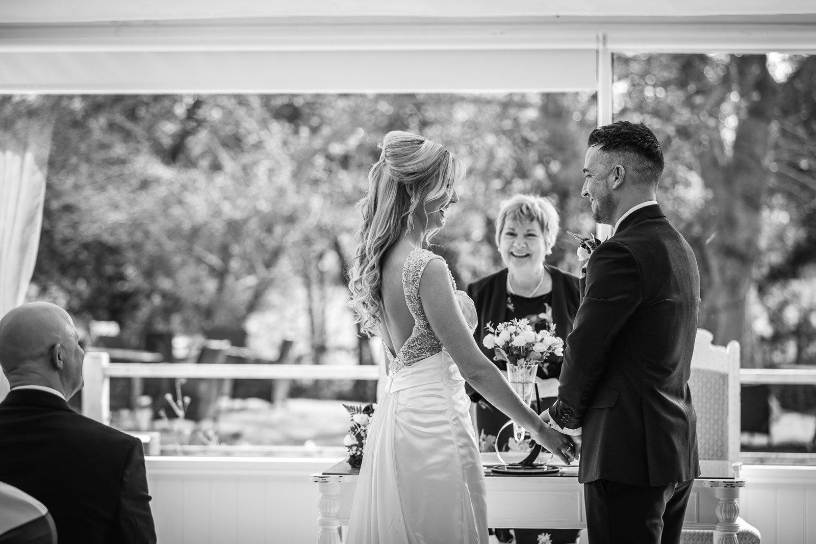 Black-and-white of the couple facing the registrar, trees beyond the window
