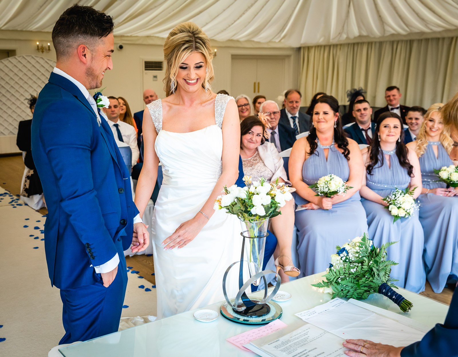 The couple standing during the ceremony, bridesmaids and guests seated behind