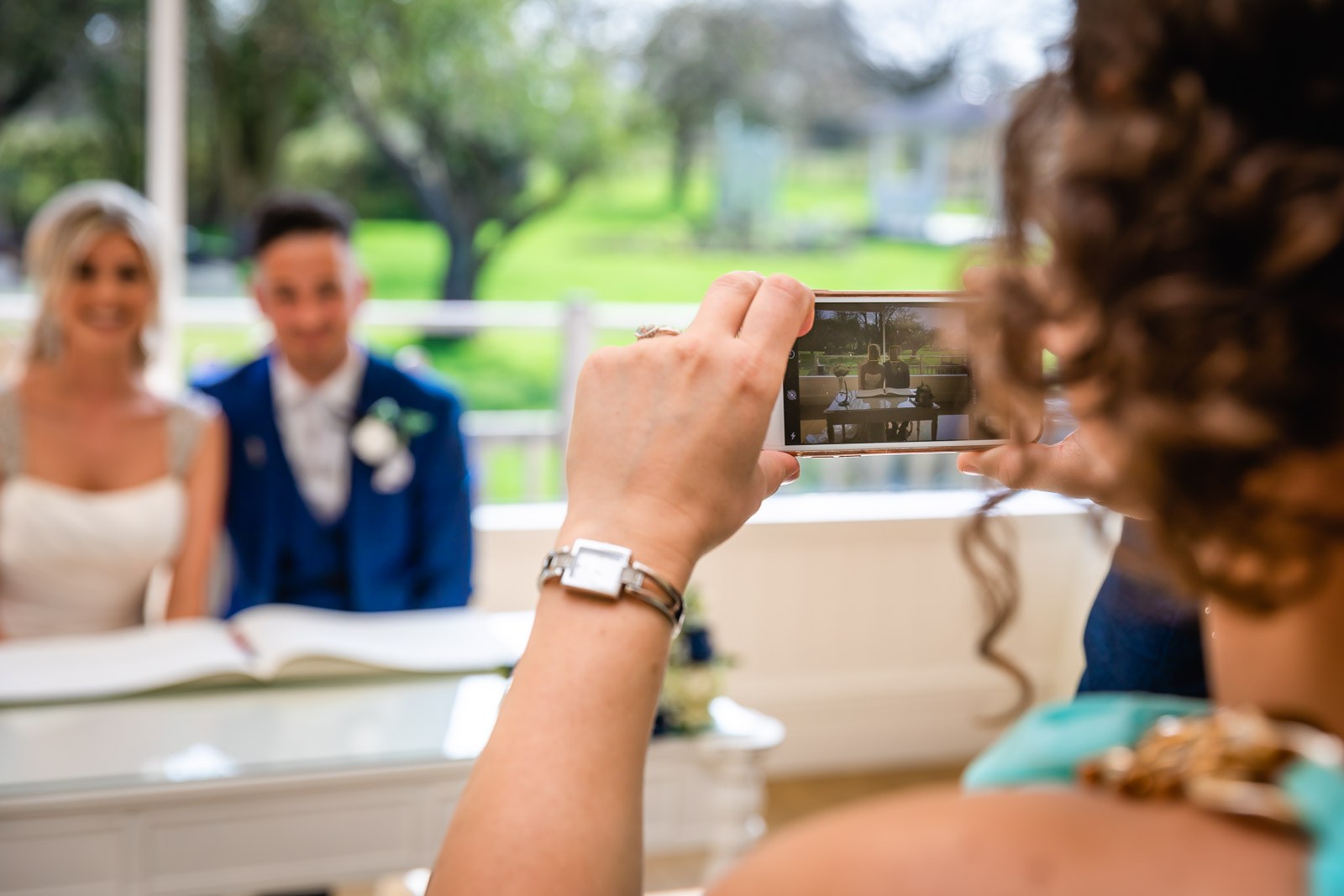 A guest photographing the couple signing the register on a phone