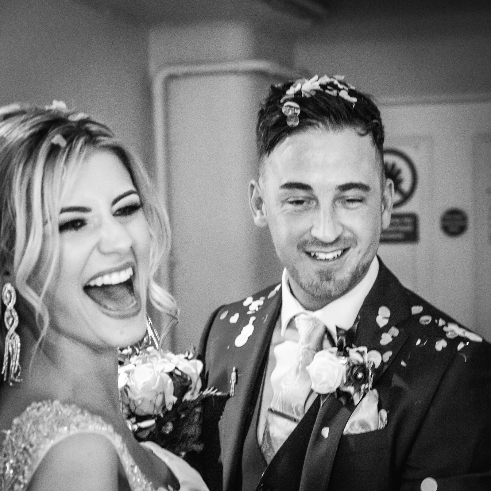 Black-and-white of the bride laughing and groom smiling amid falling confetti