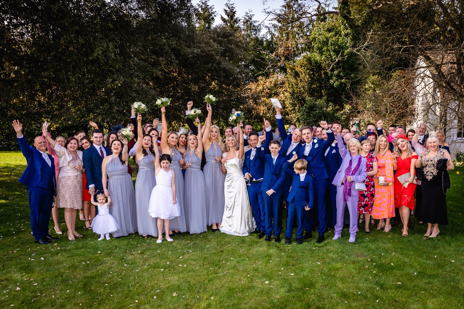 The full wedding party cheering together on the lawns at Fennes