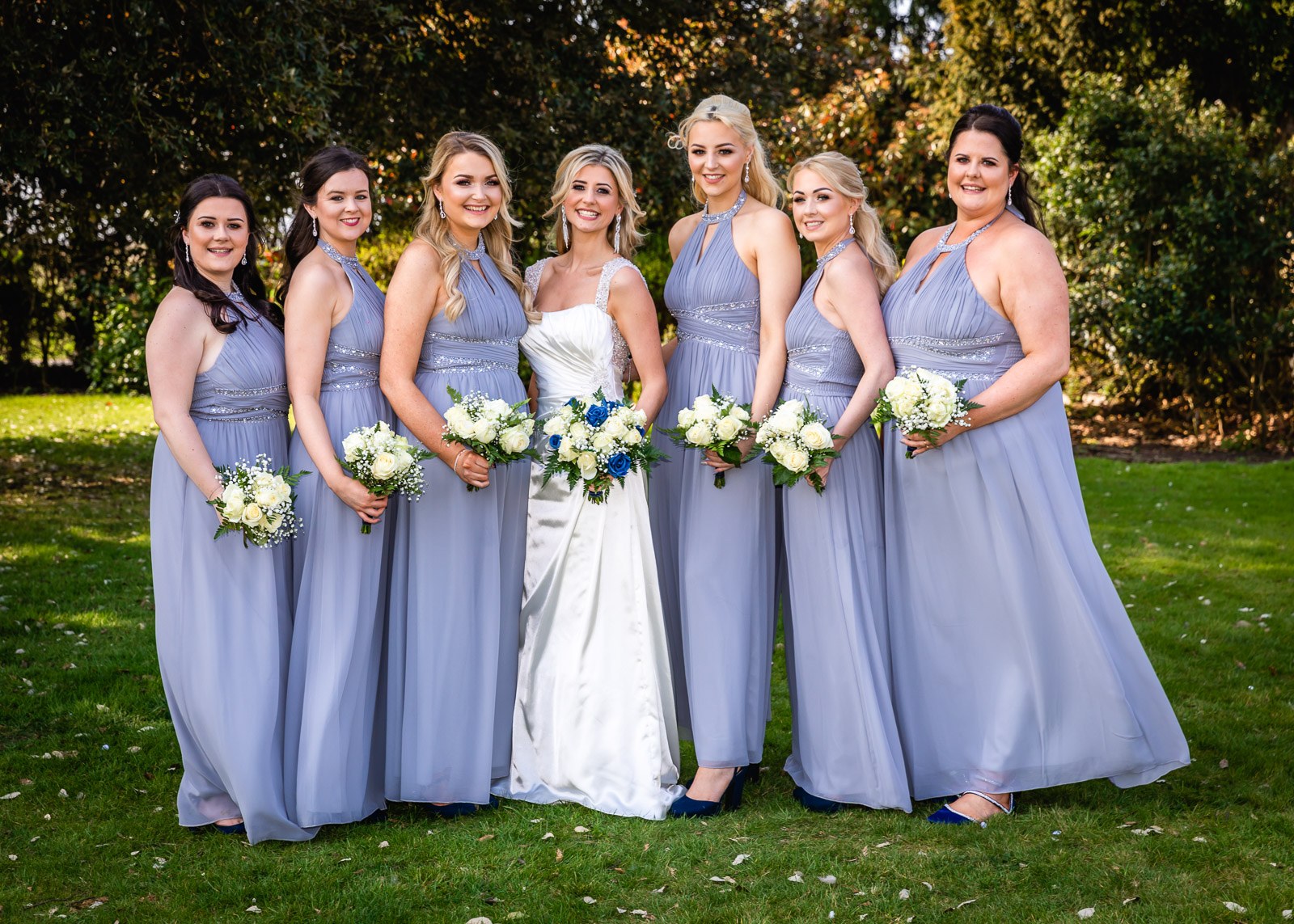 The bride with her lilac bridesmaids holding bouquets on the lawns at Fennes