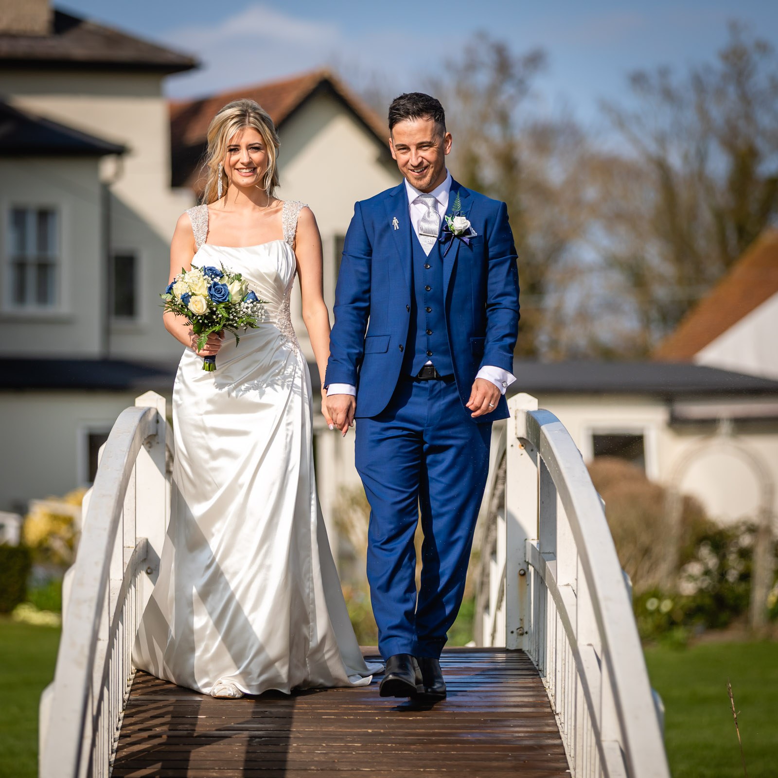 Bride and groom holding hands on the footbridge, the house at Fennes behind