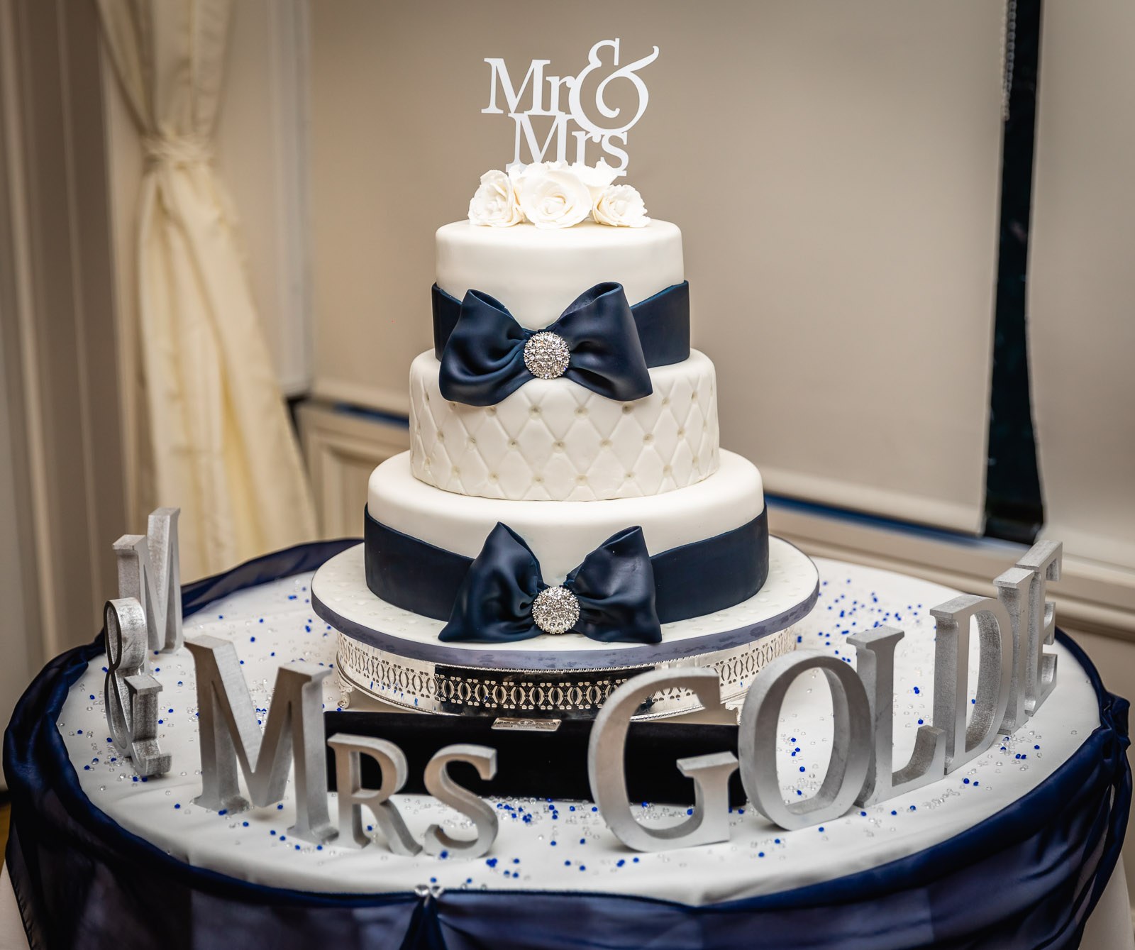 The tiered white wedding cake with navy bows and a personalised topper