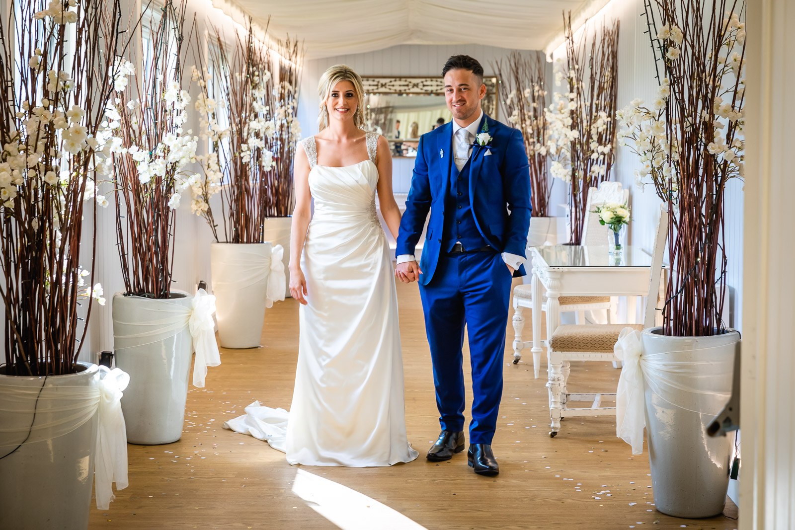 Bride and groom entering the reception at Fennes between tall blossom-branch displays