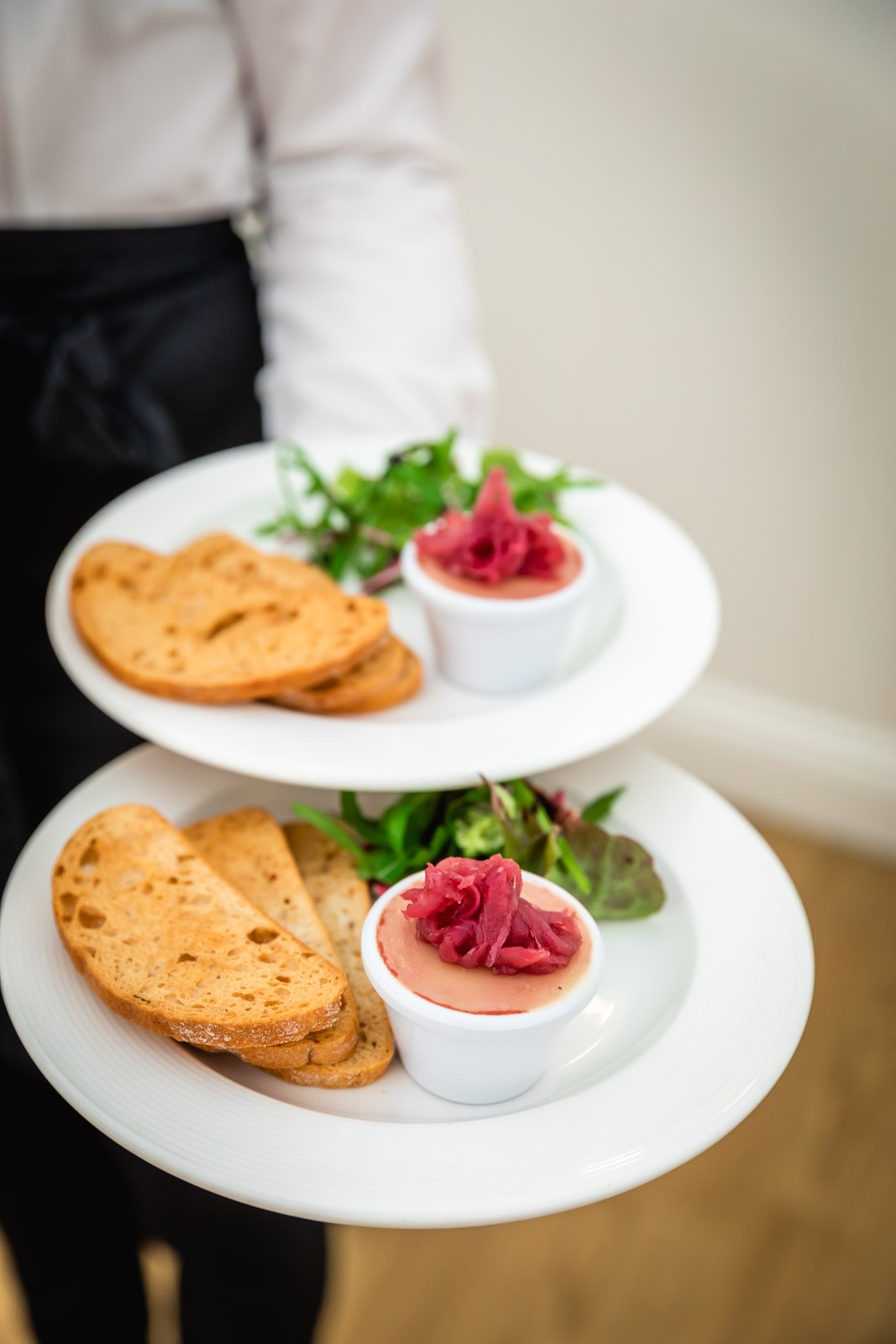 A waiter carrying a tiered plate of pate and toasted bread starters