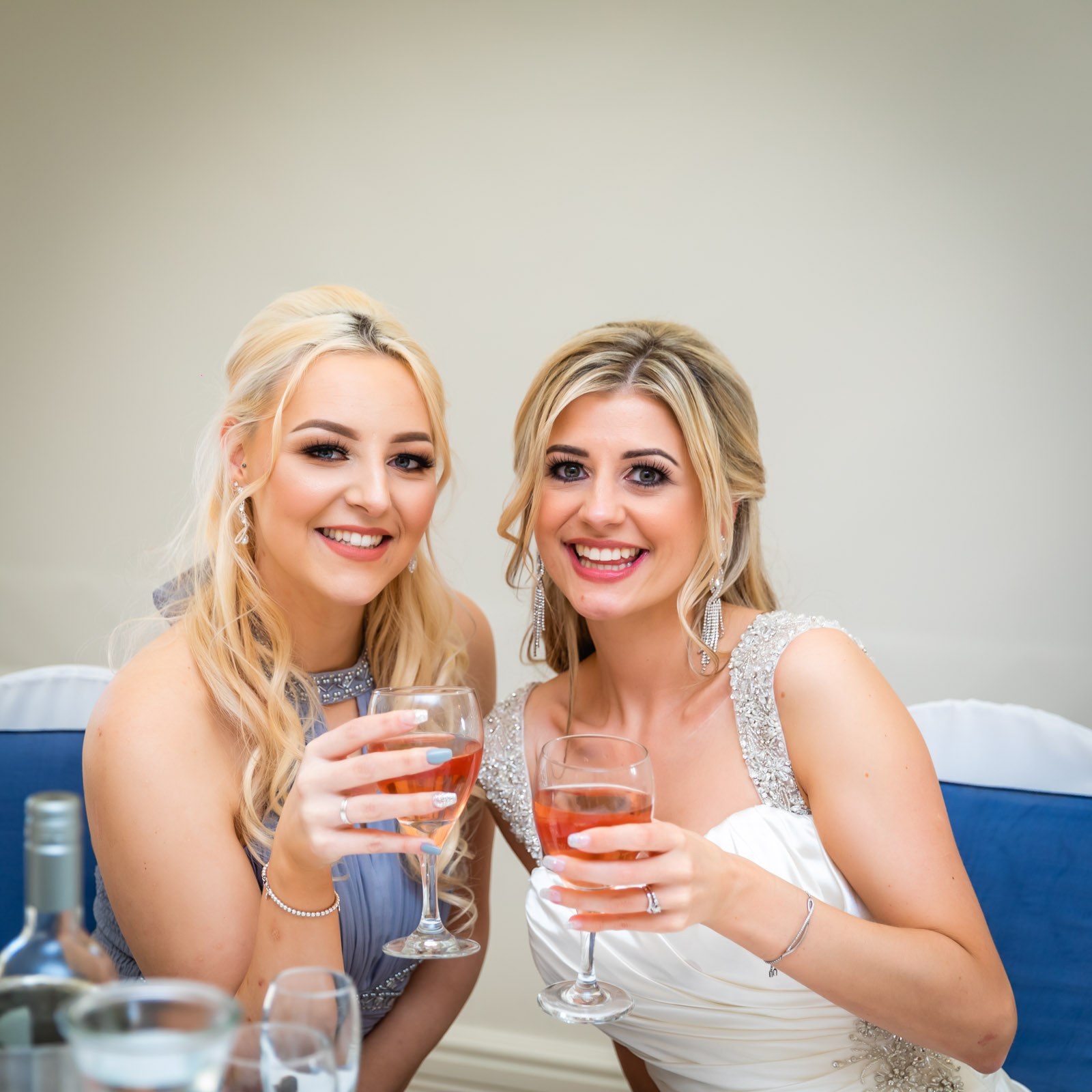 The bride and a bridesmaid smiling with glasses of rose at the table