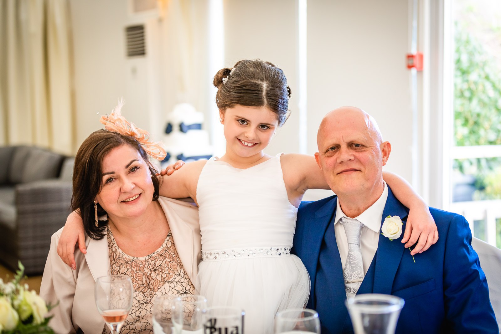 A flower girl posing between two guests at the table