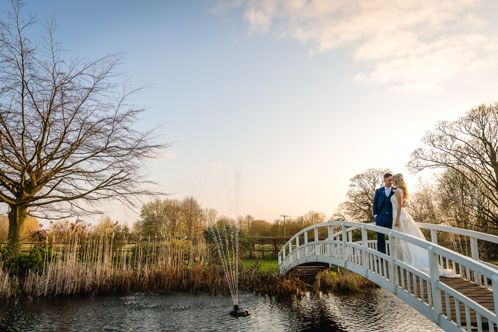 The couple on the white footbridge at sunset, the lake fountain playing at Fennes