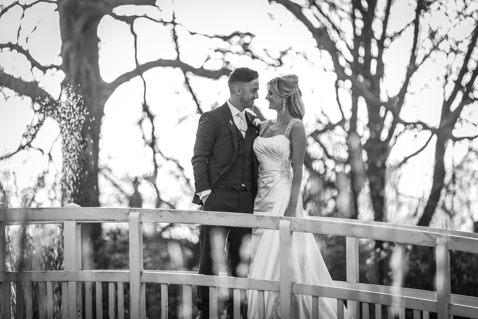 Black-and-white of the couple embracing on the bridge among bare trees