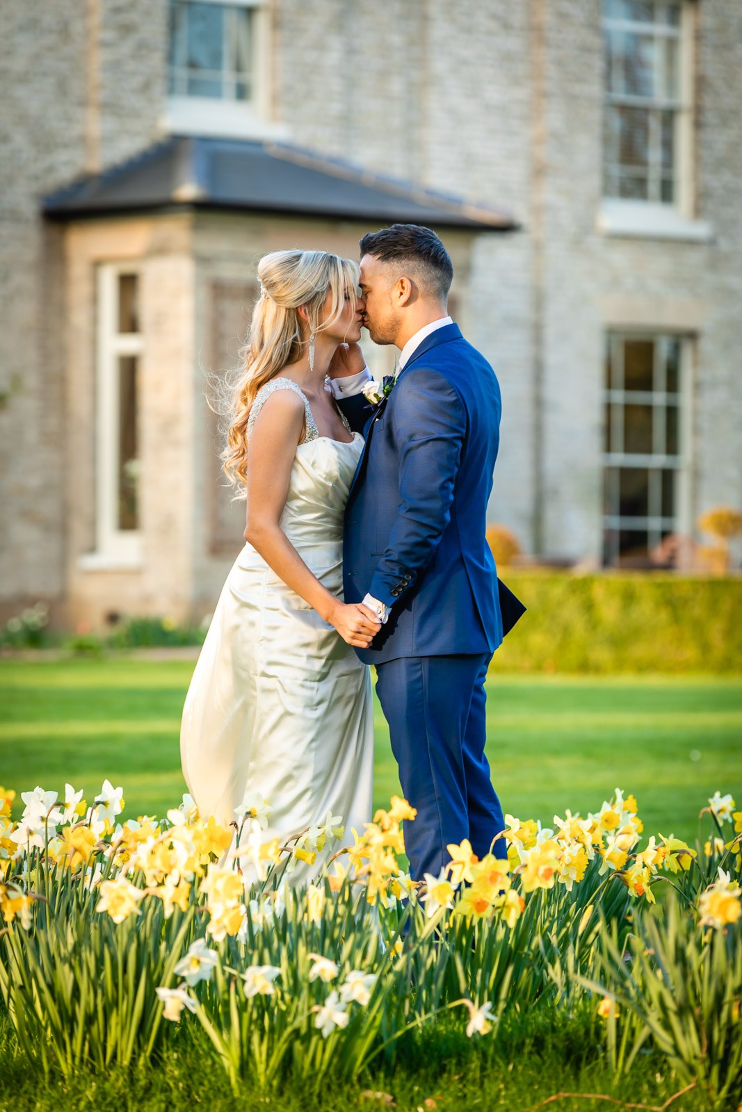 The couple kissing on the lawn among daffodils, the house at Fennes behind
