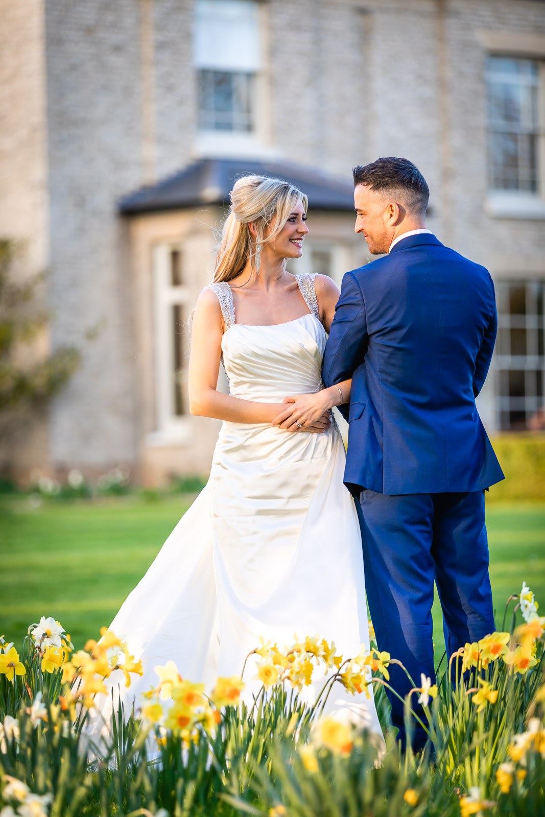 The couple embracing on the daffodil lawns of Fennes, the house behind