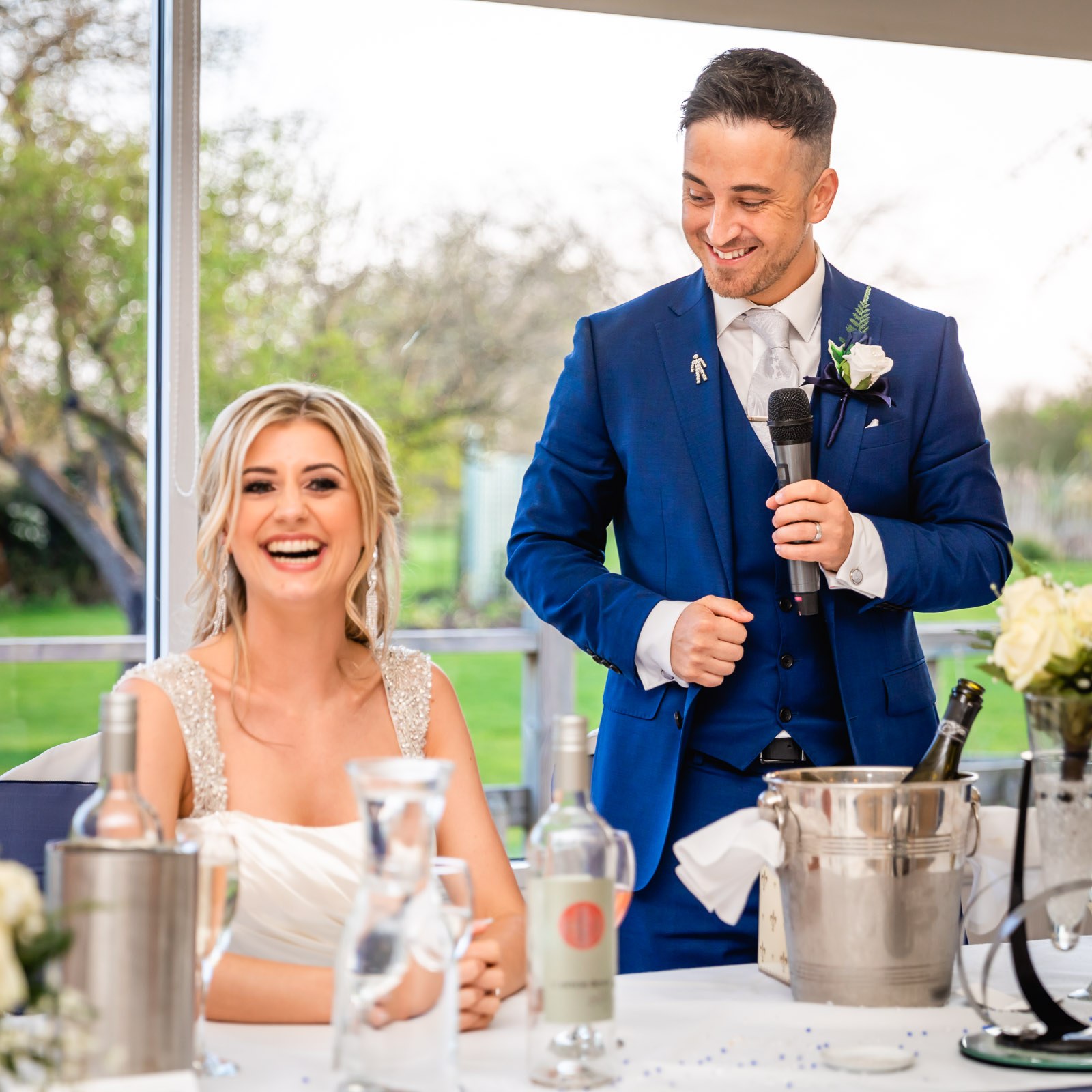 The groom giving his speech as the bride laughs beside him
