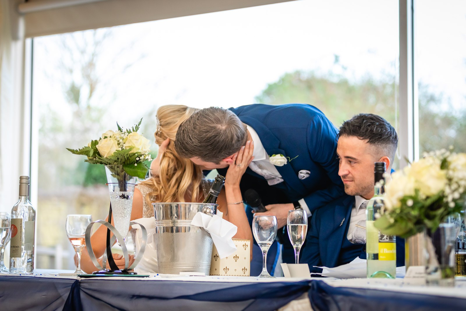 The groom kissing the bride at the top table during the speeches