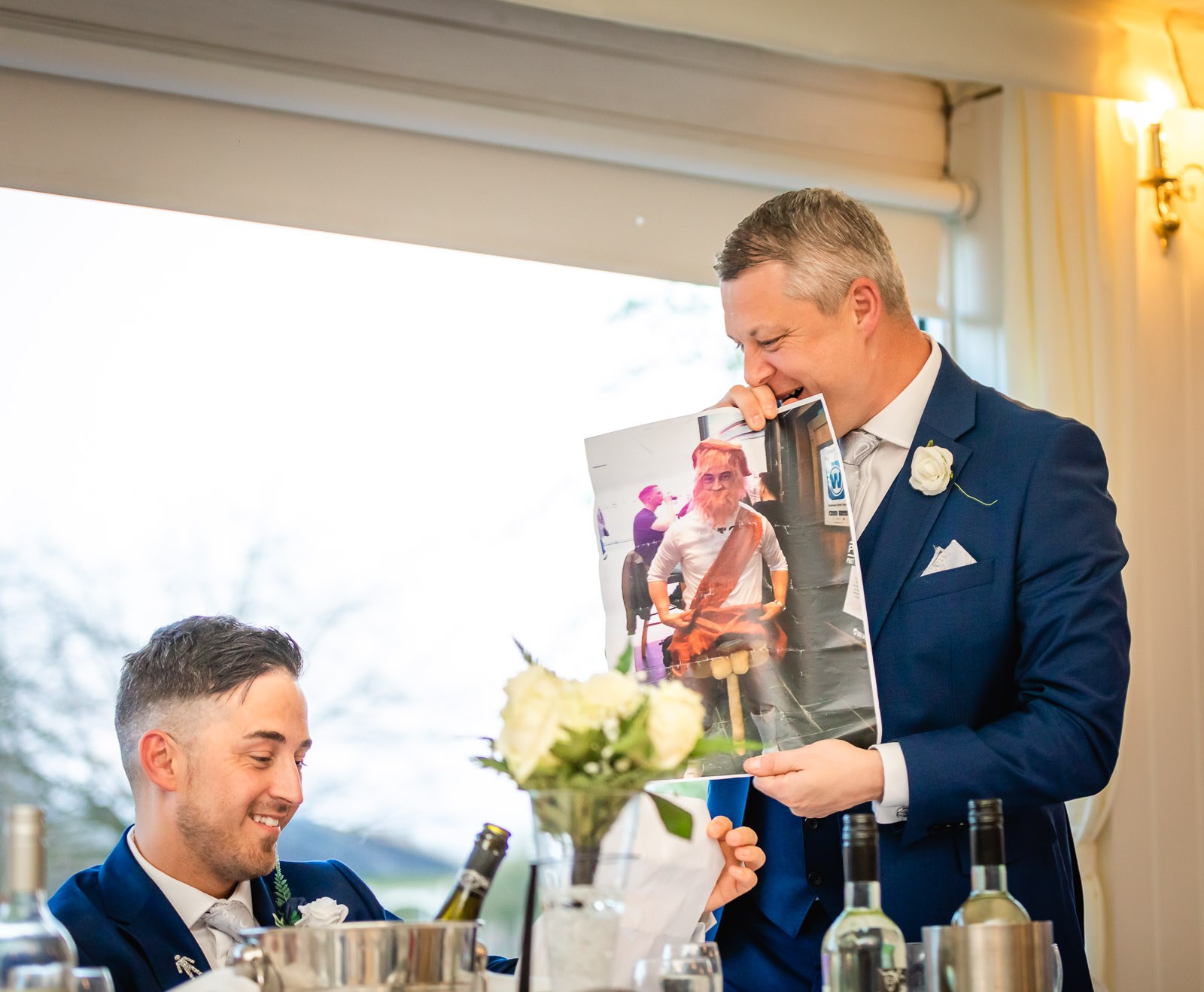 A groomsman holding up a photo prop as the groom laughs
