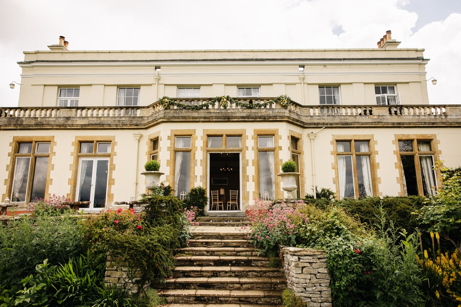 The honey-stone Georgian frontage of Glenfall House, with steps rising through summer flower borders