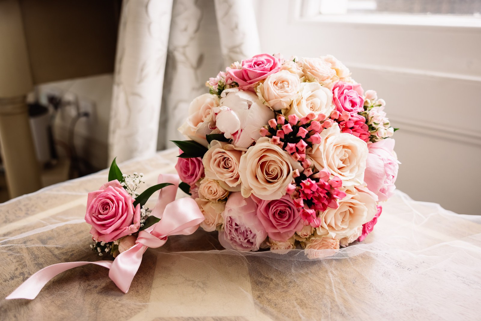 Bride's bouquet of pink and ivory roses and peonies resting on a windowsill