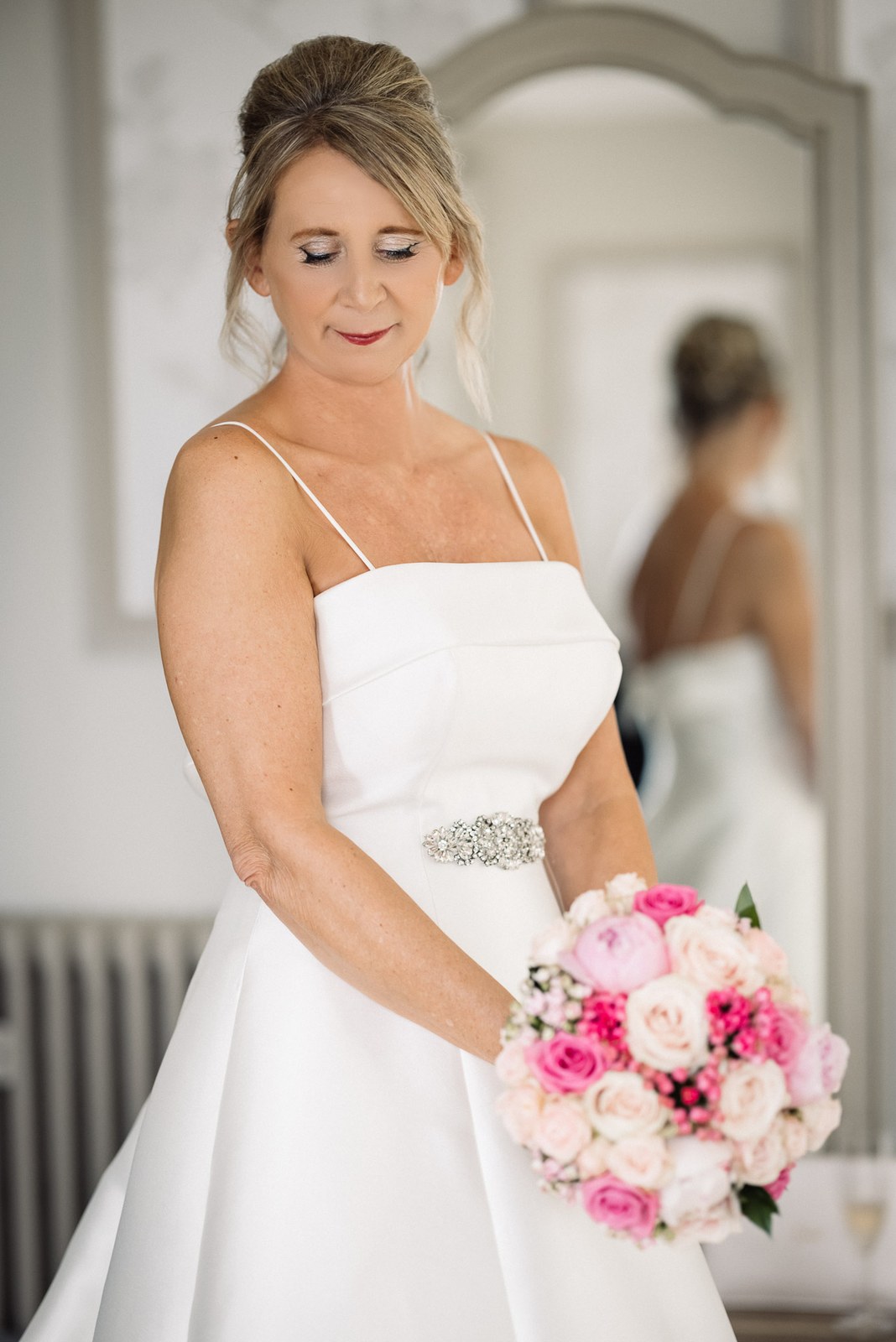 Bride in her strappy satin gown holding her pink bouquet before the wedding
