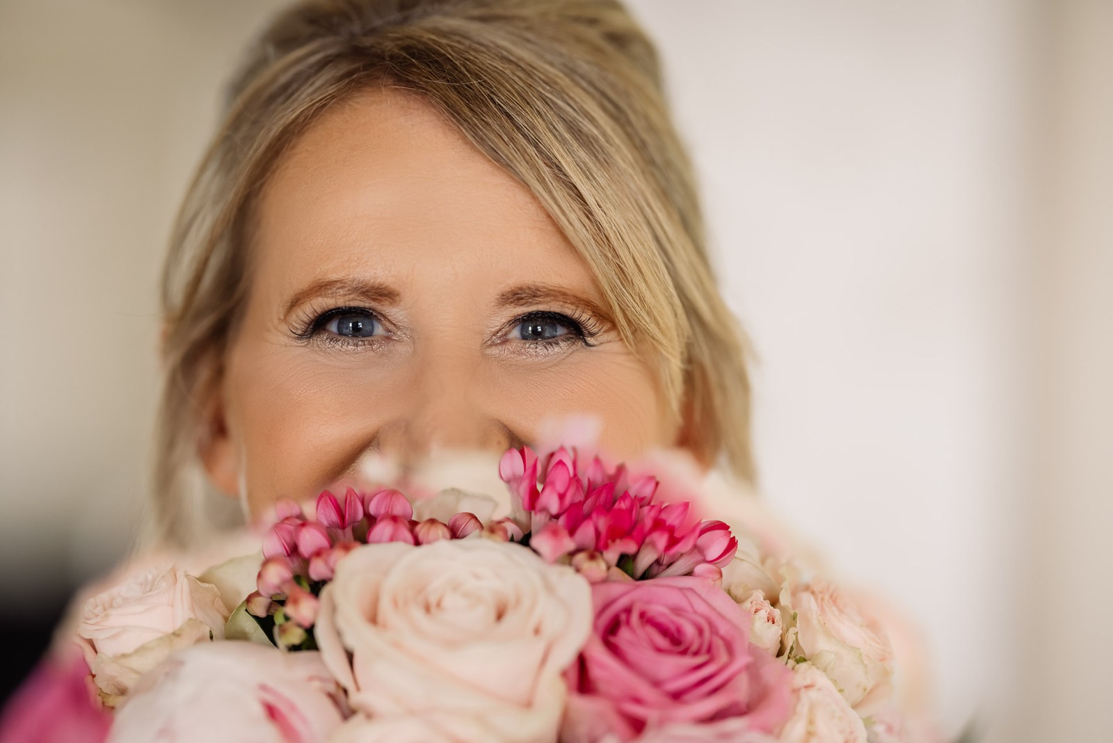 The bride's eyes peeking over her bouquet of pink and ivory roses