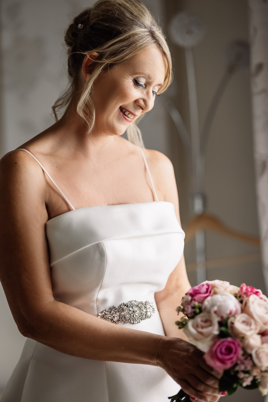 Bride looking down and smiling in her satin gown during the preparations