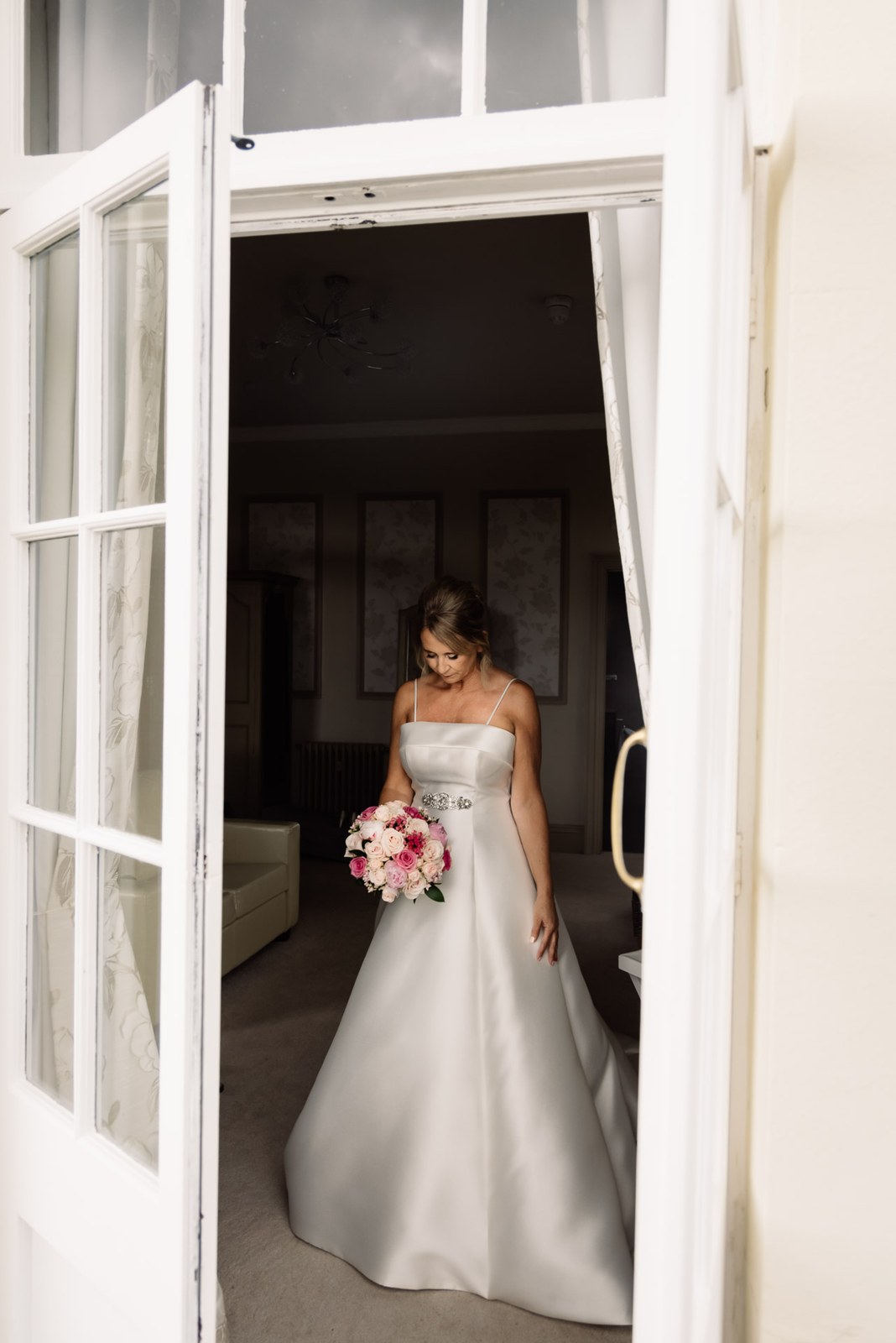 Bride framed in a bedroom doorway at Glenfall House, holding her bouquet