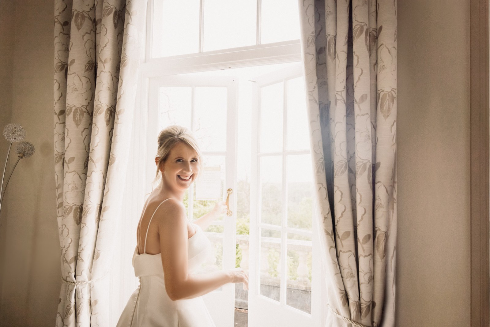 Bride glancing back over her shoulder at an open window with garden views