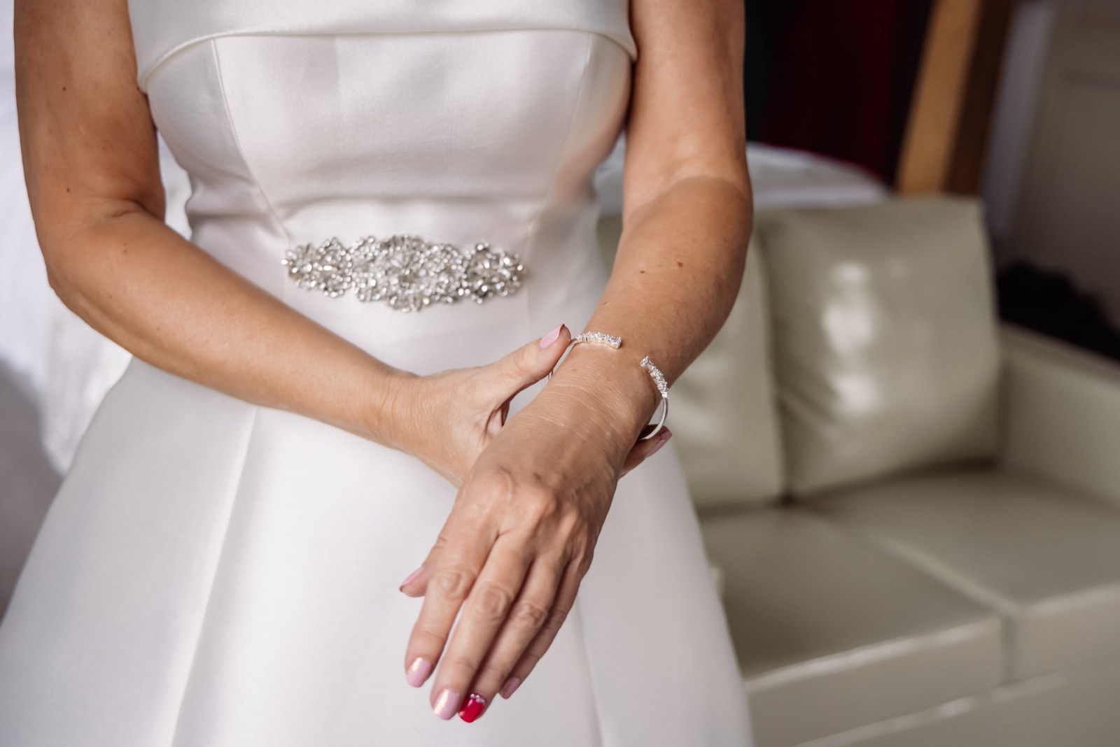 Detail of the bride's diamante belt and manicured hands against the satin gown