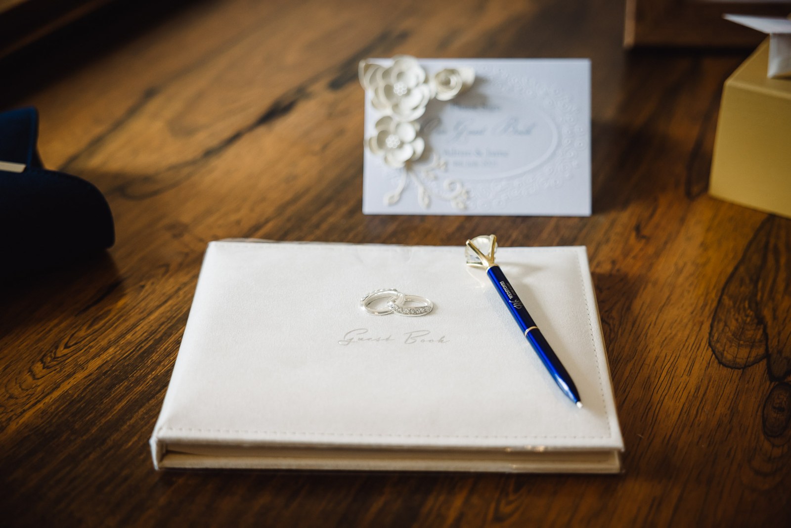 Wedding rings resting on a cream guest book beside a blue pen