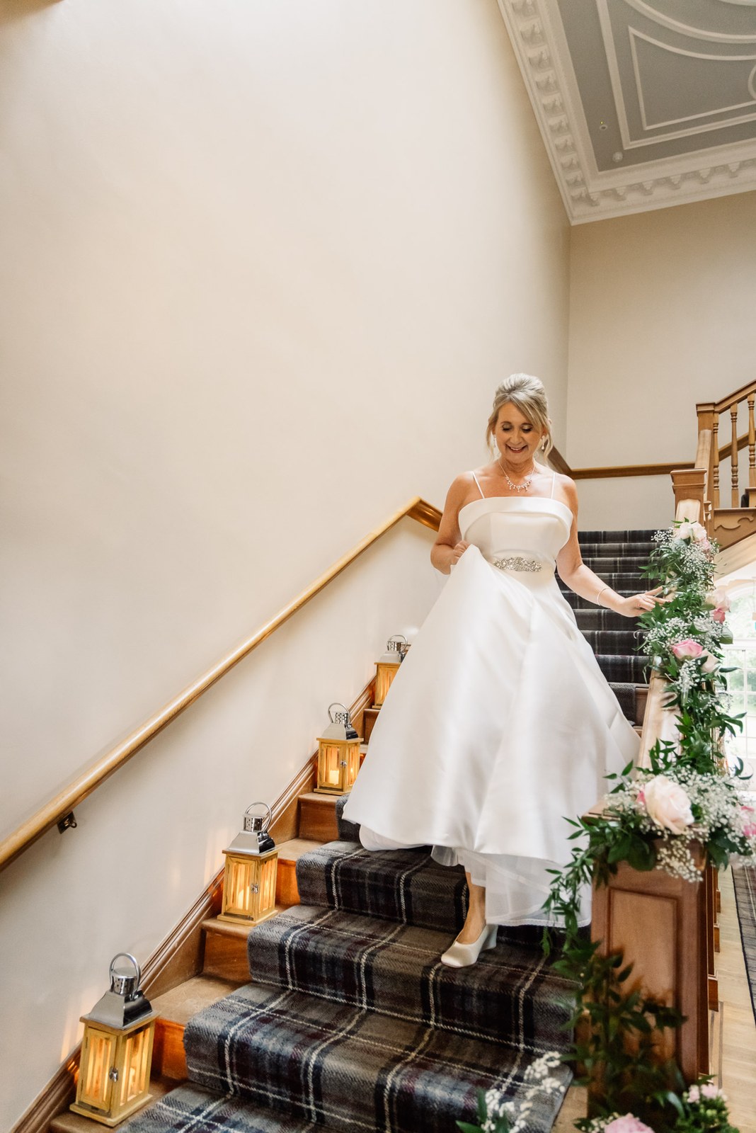 Bride descending the staircase at Glenfall House, lit by lanterns and greenery