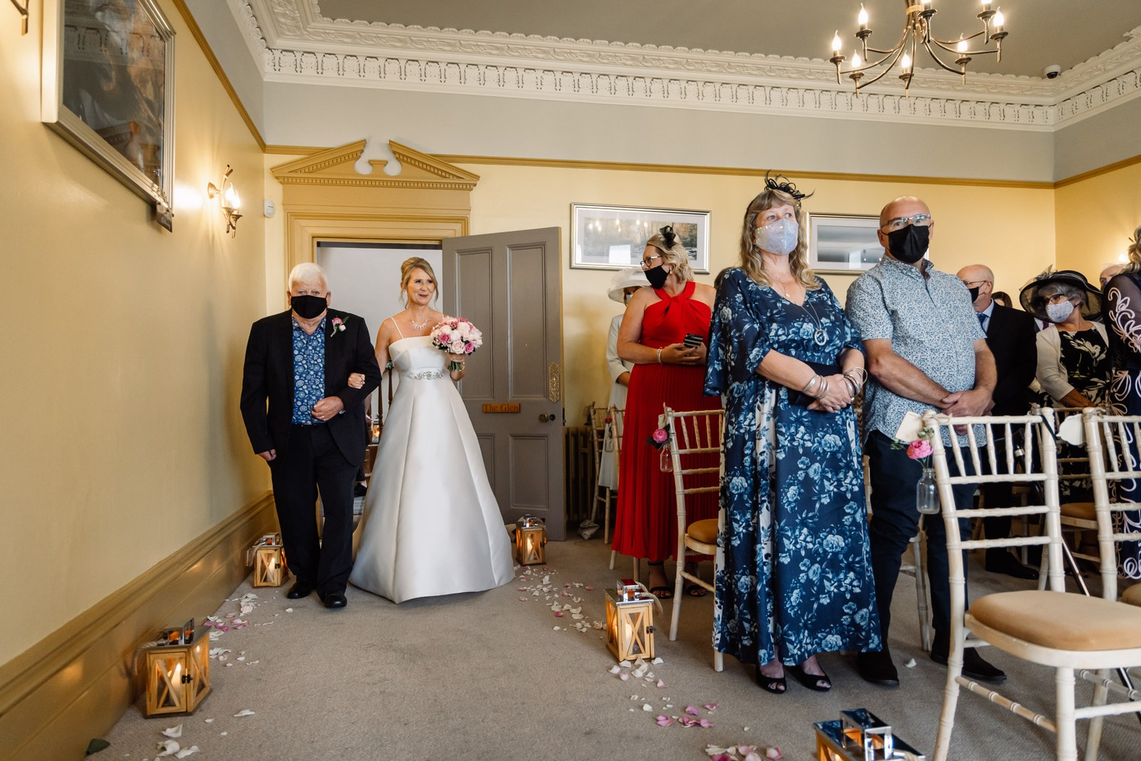 Bride and her father entering the candlelit ceremony room down a petal-strewn aisle