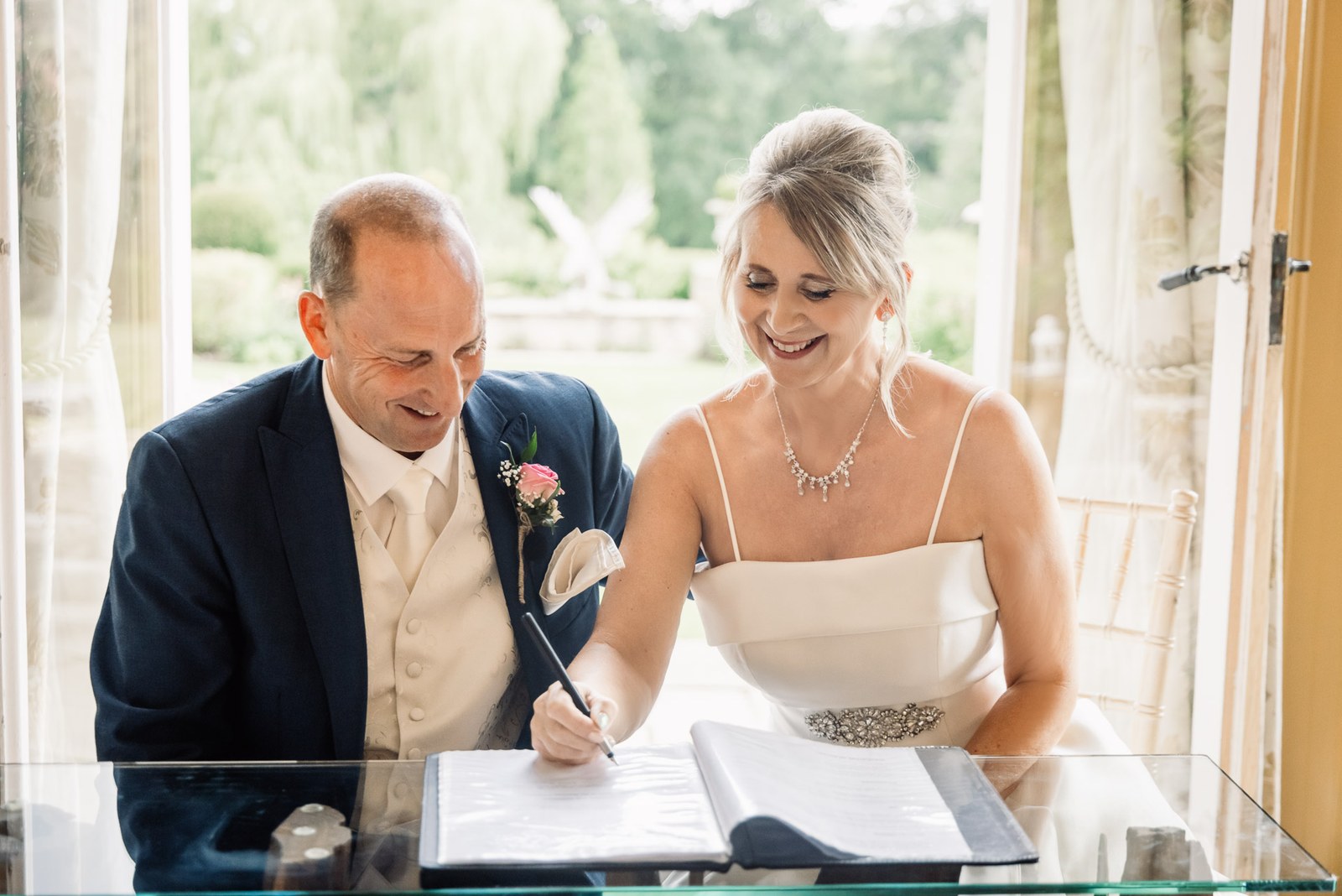 Bride and groom signing the marriage register by a garden-facing window