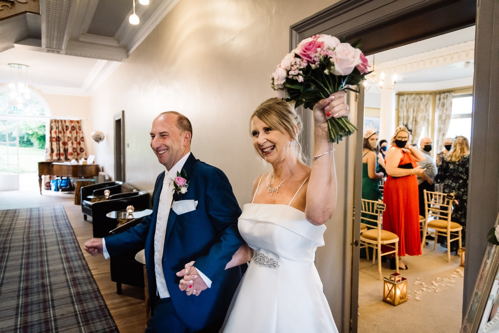The newlyweds entering the drawing room, the bride raising her bouquet in celebration