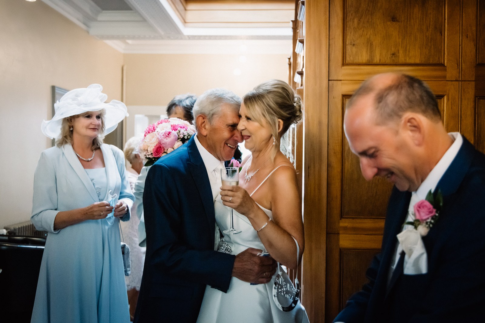 The bride embraced by a guest over champagne after the ceremony, the groom nearby